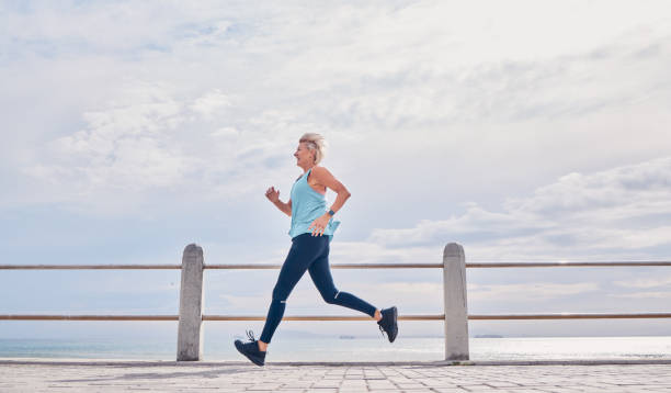 donna senior che corre all'aperto al mockup on sky sul lungomare per l'energia, la salute e l'allenamento cardio. donna anziana, esercizio fisico e corridore all'oceano per allenamento sportivo, fitness e maratona sana - endurance sport foto e immagini stock