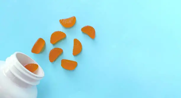 Photo of Blue background with vitamin C gummies in the form of orange slices. Space for text
