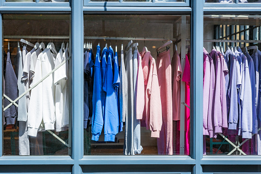 A selection of cotton shirts in a variety of colors hanging in the window of a clothing store.