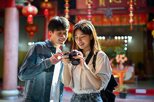 Happy and smiling young Asian tourist couple enjoying their old town sightseeing, taking photos and visiting a Chinese temple together.