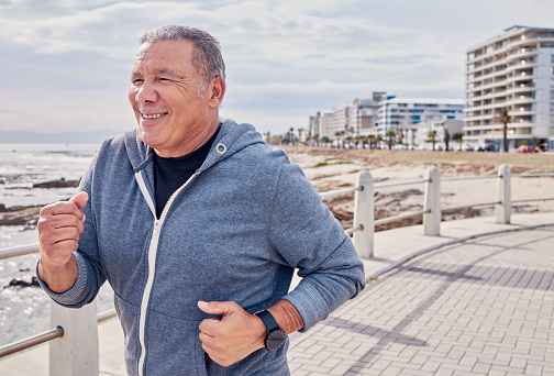 Senior man, fitness and running at ocean sidewalk for energy, wellness or workout in Miami. Elderly male, cardio exercise and happy runner at seaside promenade of training, sports and smile of action