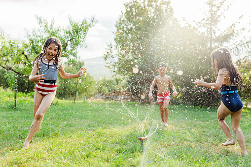 Group of children having fun with garden sprinkler in the yard