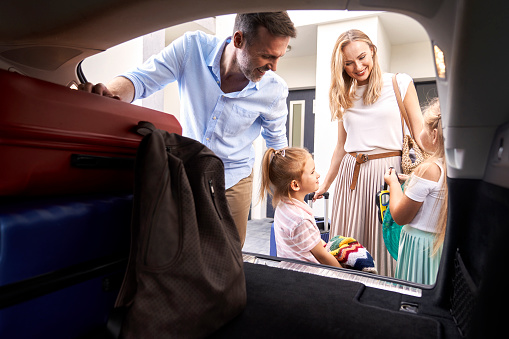 Caucasian family of four packing luggage into car trunk for holiday