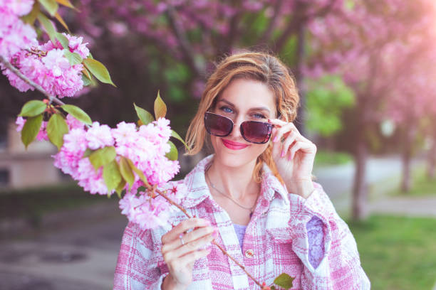 istock Young beautiful woman taking off sunglasses and looking into camera during springtime blooming 1491217262