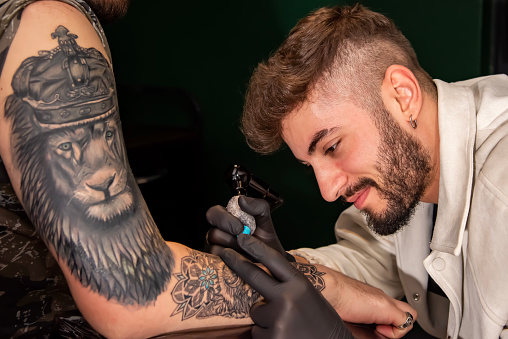 Professional tattooer doing tattoo on hand using tattoo machine in studio
