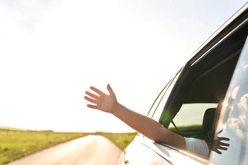 Unrecognizable child showing hand out of running car