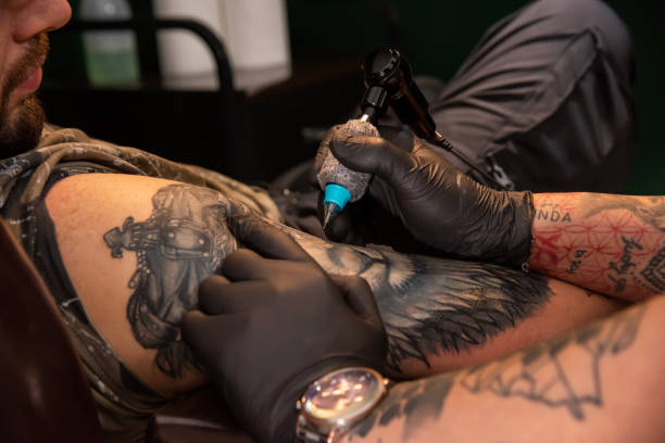 istock Professional tattooer doing tattoo on hand using tattoo machine in studio 1491219650