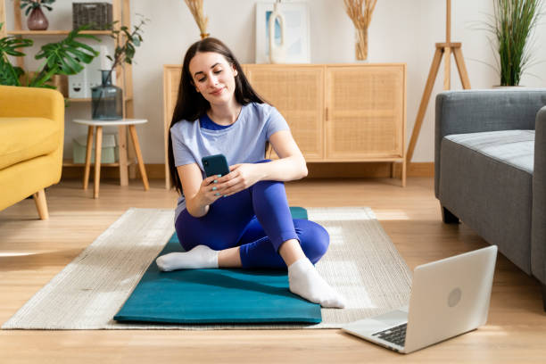 istock Woman sitting on exercise mat using mobile phone. 1491224276