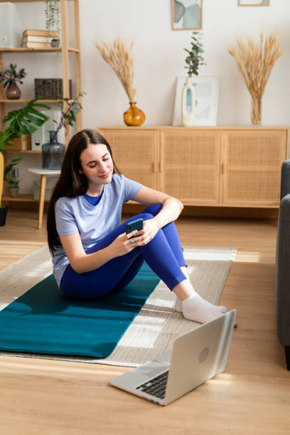 istock Woman sitting on exercise mat using mobile phone. 1491224407