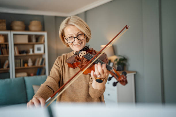 A retired woman plays the violin in the living room at home, spending her retirement days enjoying her new hobby. stock photo