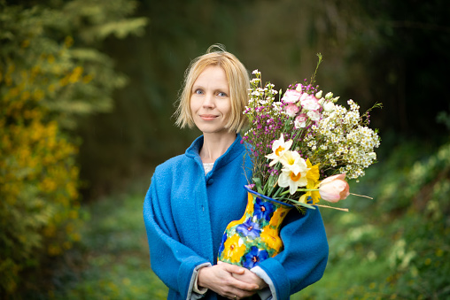 Woman with a bouquet in the forest. Blue coat and green forest background. Alone with nature.