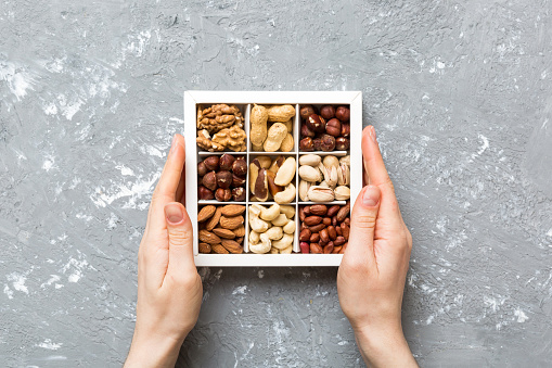 Young woman holding box with different nuts, closeup. Close up, copy space, top view, flat lay. Walnut, pistachios, almonds, hazelnuts and cashews.