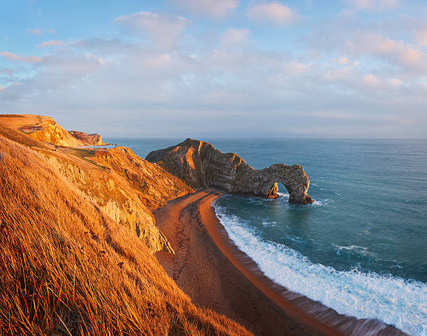 Durdle Door The well known geological landmark on the Jurassic coast in Devon shot in beautiful warm evening light and as a three shot vertical stitch, giving a view back to Lulworth on this large file. Delicate clouds stretch across a blue expansive sky. devon stock pictures, royalty-free photos & images