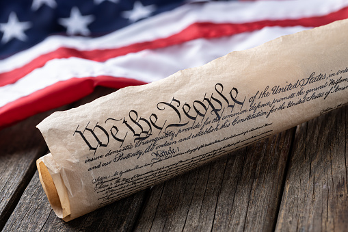 United States constitution with American flag in background on rustic wooden table