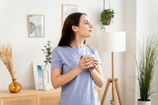 Woman drinking a cup of coffee at home, eyes closed enjoying the aroma.