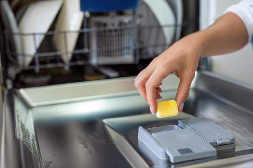 Hand loads a dishwashing tablet into dishwasher