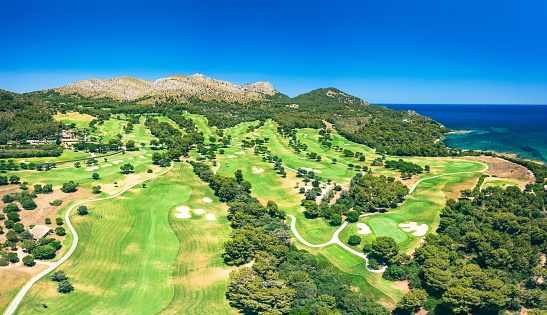 Green golf court near the mountain and sea, aerial view.