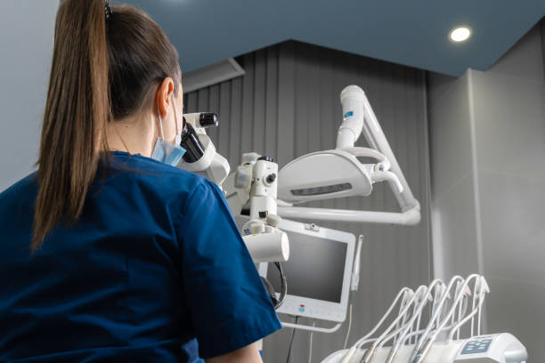 istock Female dentist using dental microscope treating patient teeth dental clinic office. undergoing treatment by experienced dentist using microscope. Image of woman on patient's chair in dentist's office. 1491245574