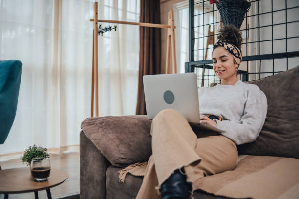 istock Beautiful young woman with curly hair using laptop while sitting on sofa at home 1491247449