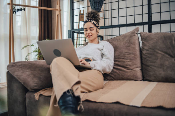 istock Beautiful young woman with curly hair using laptop while sitting on sofa at home 1491247530