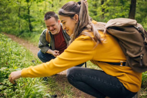Two friends, a young woman and man with Down syndrom, hiking together in the forest Two friends, a young woman and man with Down syndrome, hiking together in the forest disabled person hiking outdoors stock pictures, royalty-free photos & images