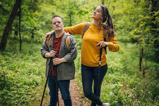 Two friends, a young woman and man with Down syndrome, hiking together in the forest