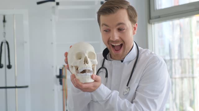 A doctor holds a model of an anatomical human skull in his office. The neurologist is having fun