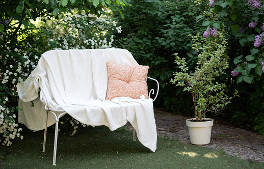 forged white metal bench in the garden with a blanket and a pillow