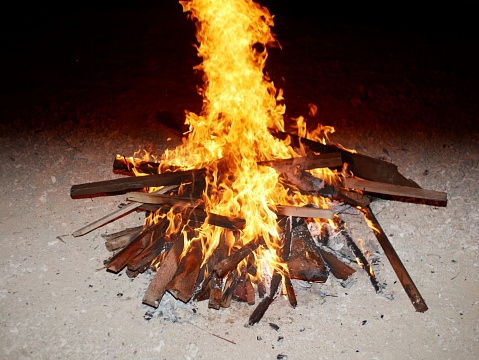 Burning wood at night. Campfire at touristic camp at nature in mountains. Flame amd fire sparks on dark abstract background. Cooking barbecue outdoor. Hellish fire element. Fuel, power and energy