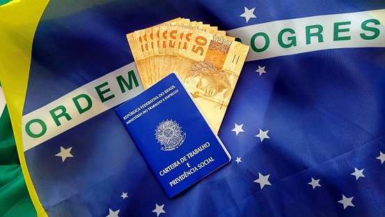 Brazilian work and social security document (Carteira de Trabalho e Previdencia Social) with brazilian money on a brazilian flag
