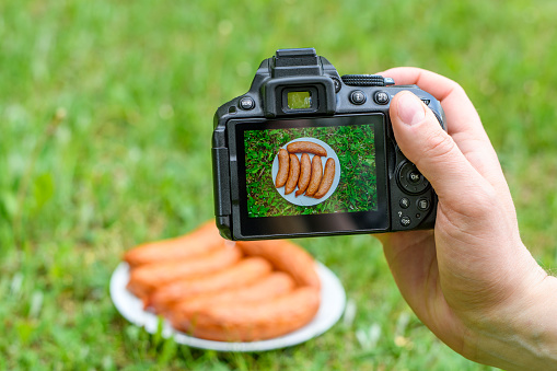 Barbecue sausage on the camera screen and lying on a plate on the grass outdoors, Double shot