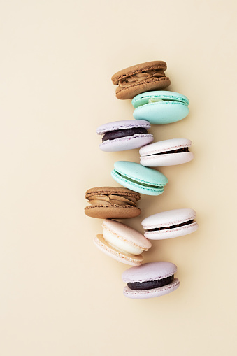 Different pastel colors pastry macarons top view on a beige background.
