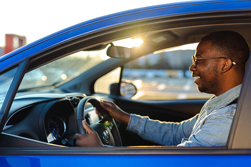 Smiling African-American man in holding the steering wheel and smiling while driving a car, on a nice sunny day
