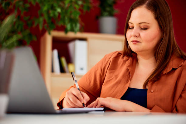 istock A hardworking plus-size woman working over a laptop and writing notes. 1491270872