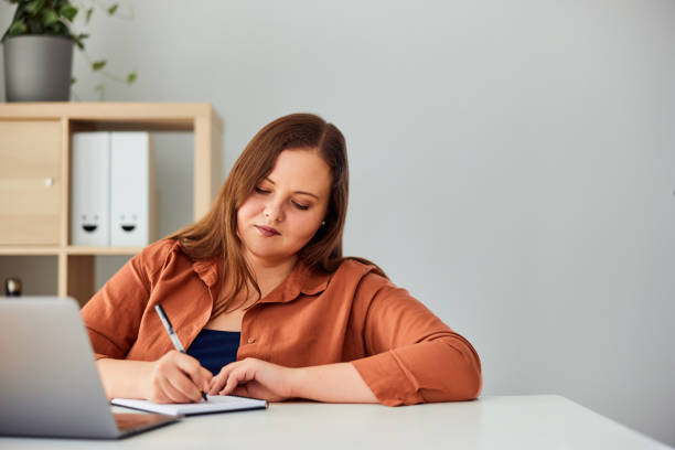 istock An ambitious curvy businesswoman writing notes and working on a laptop. 1491271359