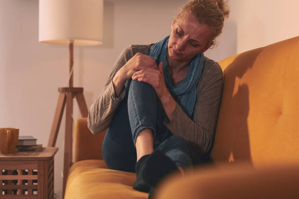 Woman with knee pain sitting on a sofa at home. stock photo