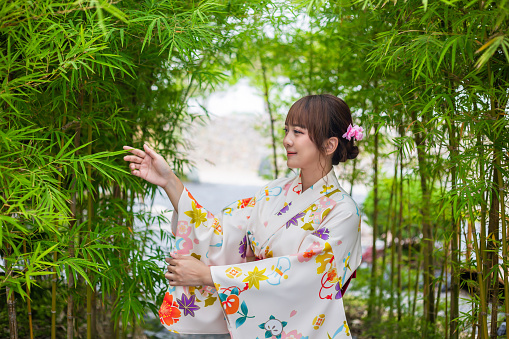 Young woman wearing traditional Japanese kimono or yukata stand in garden with bamboo trees.