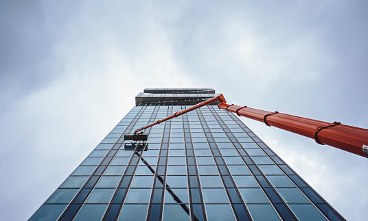 Cleaner worker using a cherry picker to clean a glas facade of a contemporary office building