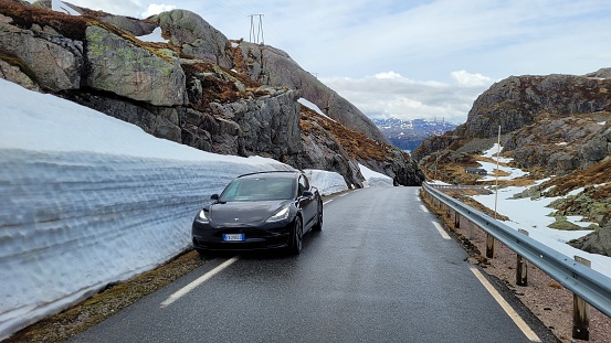 Lysebotn, Norway - May 31, 2022: Wonderful landscapes on the road in Norway. Lysebotn surroundings snowy scenic view. A static shot of a Tesla Model 3 electric car. Snowed mountains. Selective focus