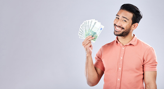Asian man, portrait and money fan on isolated background for financial freedom, stock market profit or investment. Smile, happy and trader cash on studio mockup for finance success, savings or growth