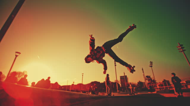 SLOW MOTION of woman doing backflip while roller skating. Female is practicing stunt at skateboard park. She is wearing helmet and kneepads.