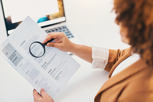 Hands, cv paper and magnifying glass at hr office with black woman, recruitment or focus at desk. Human resources, documents or zoom for hiring, opportunity or job for future employee with inspection