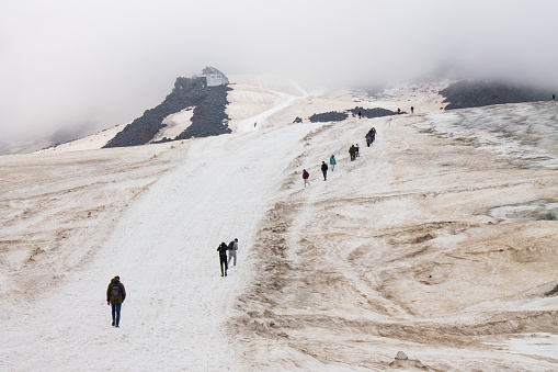 Tourists climb the snowy road to Elbrus among the fog and cloudy sky in the northern Caucasus in russia and copy space