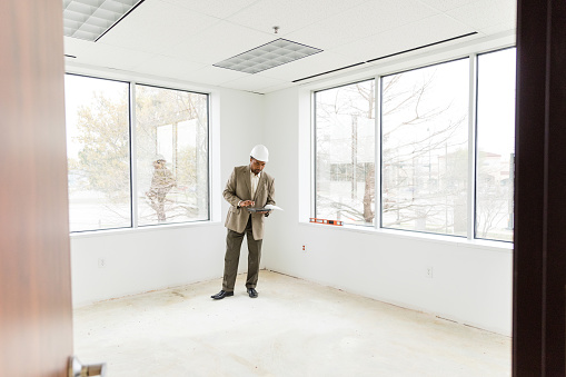 While inspecting the empty office space, the male business owner reads plans on his digital tablet.