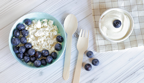Healthy breakfast. Cottage cheese with blueberries, top view. Healthy keto breakfast concept, fresh berries and cottage cheese with sour cream. Plate with healthy breakfast and wooden spoon and fork