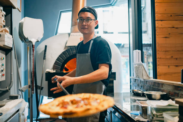 istock An Asian man is working in the restaurant kitchen, using a wood-fired oven to prepare traditional pizzas. 1491289803