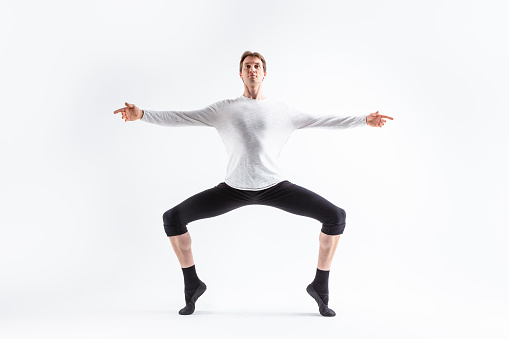 Handsome Young Man Dancing Ballet Posing in Stretching Pose with Lifted Hands in White Shirt On White. Horizontal Image