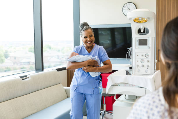 Smiling female doctor carries baby to unrecognizable new mother The smiling senior adult female doctor carries the newborn to the unrecognizable new mom. Midwife stock pictures, royalty-free photos & images