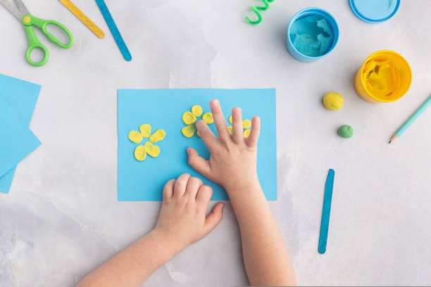 Blue and yellow flowers from plasticine. Kid's craft. Child's hands with dough clay. Colorful clay stock photo