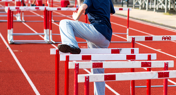 Rear view of one high school girl performing hurdle drills warming up for a race outdoors.